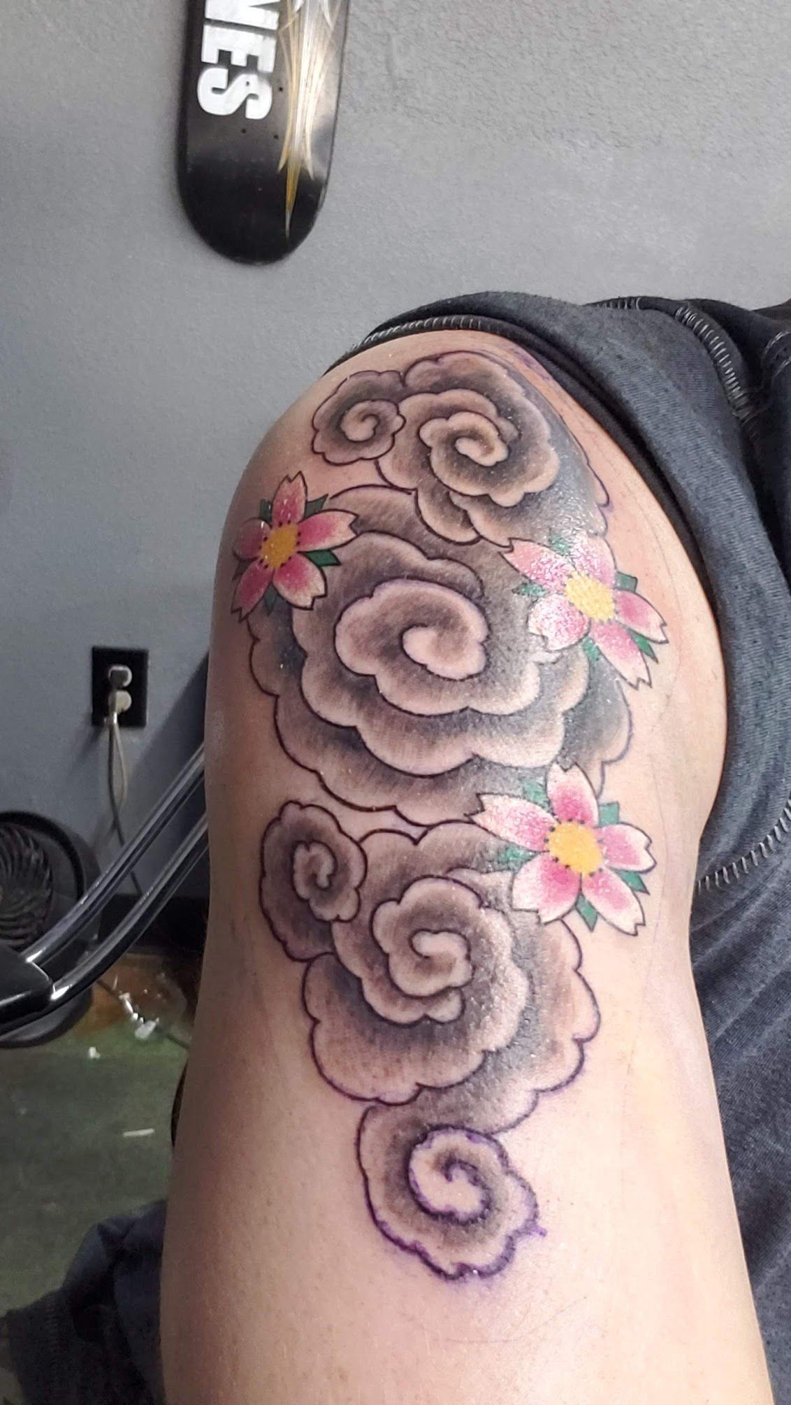 A person has a tattoo of clouds and flowers on their knee.