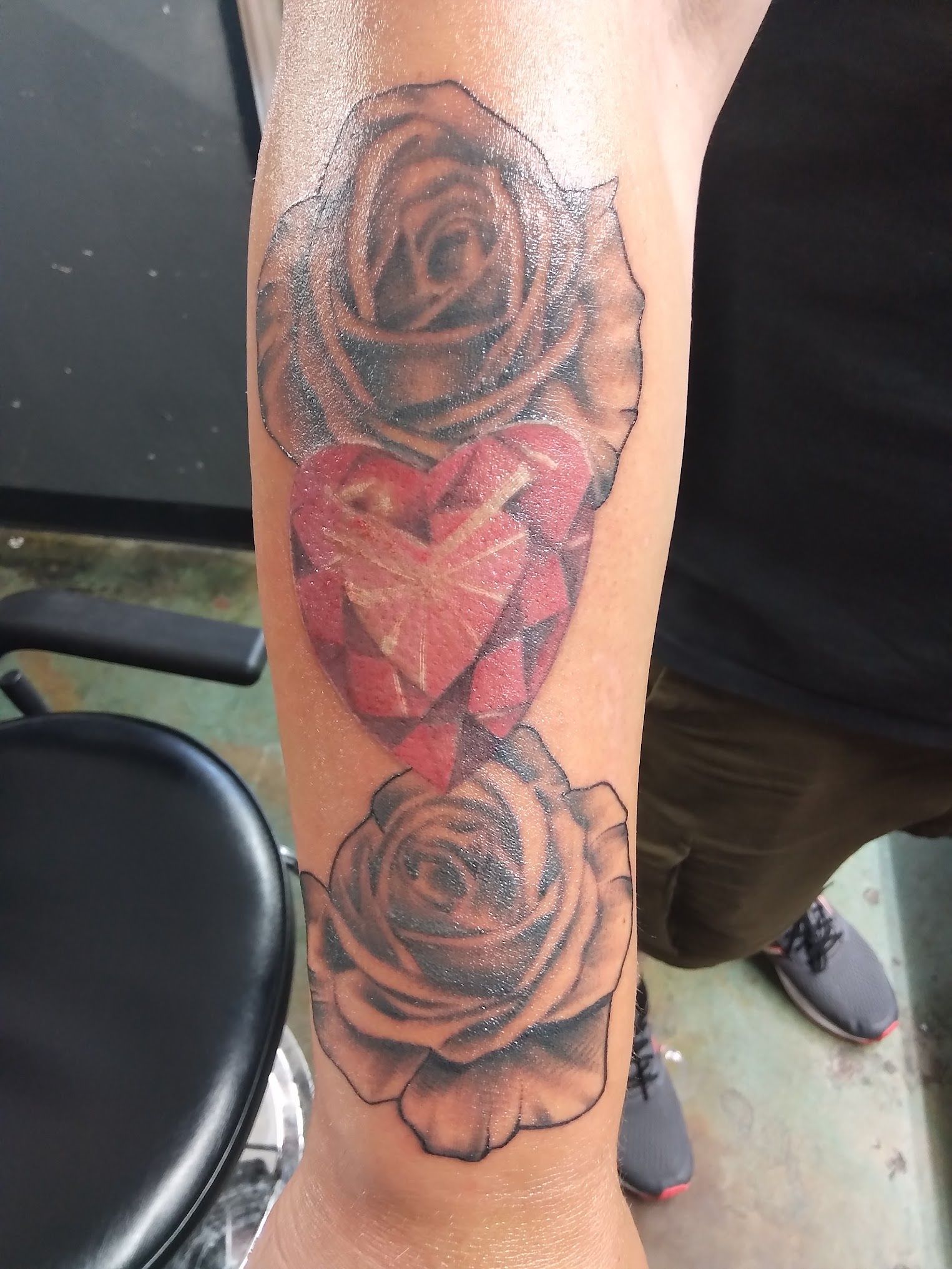 A person has a tattoo of two roses and a heart on their arm.