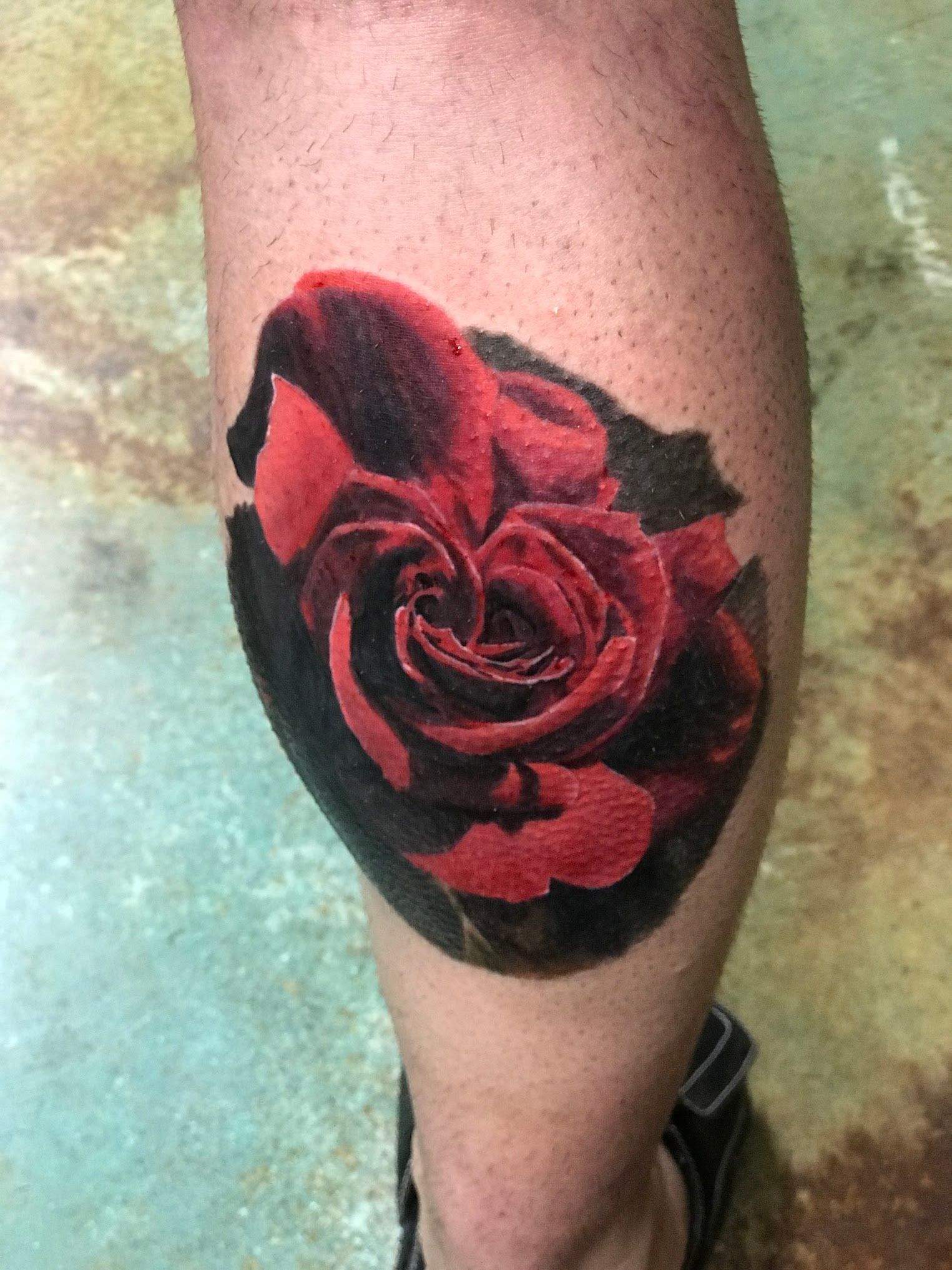 A person has a tattoo of a red rose on their leg.