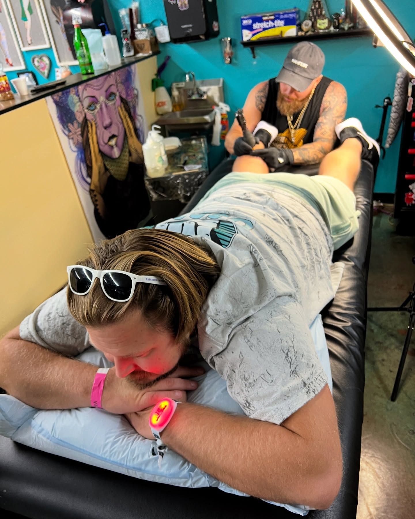 A man is laying on a bed getting a tattoo on his leg