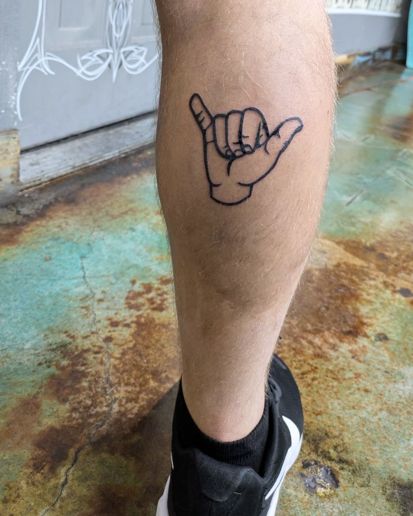 A person has a tattoo of a hang loose hand sign on their leg.