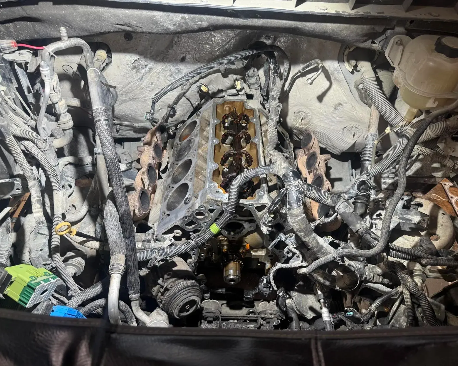 An open engine bay with the cylinder head removed, revealing the engine block, pistons, and complex wiring harness.