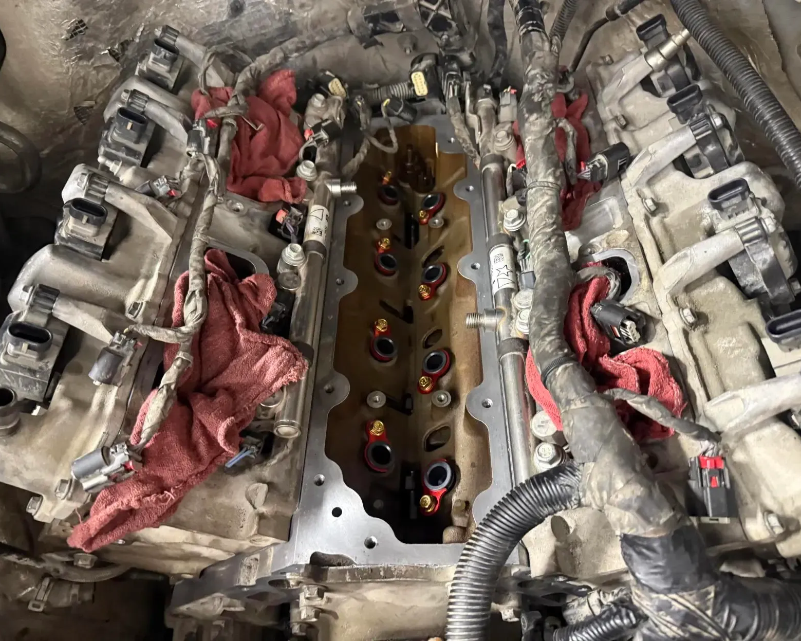 An open car engine bay showing a cylinder head with exposed valves and red rags stuffed into intake ports.