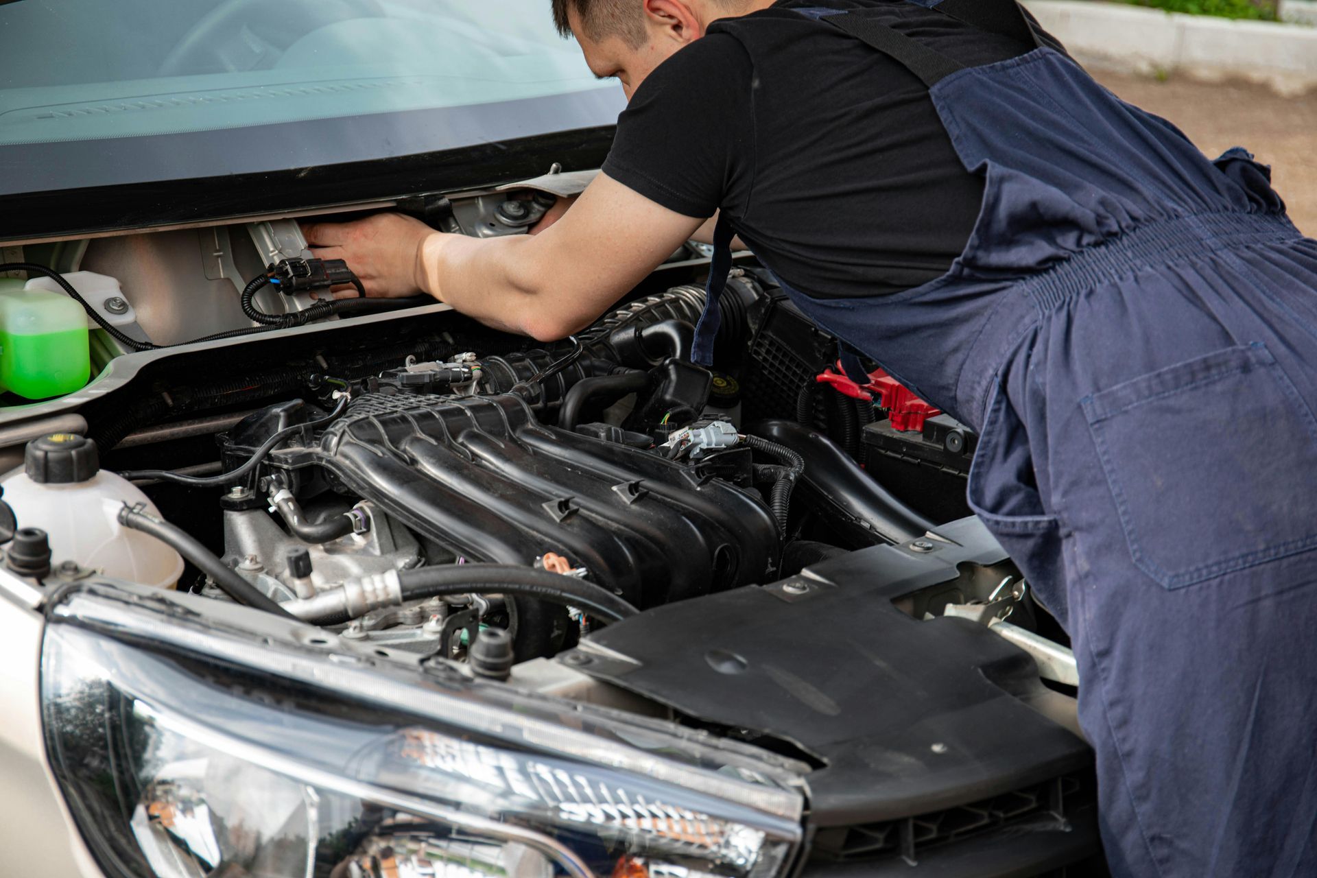 A mechanic in dark blue coveralls works on the engine of a vehicle under the hood.