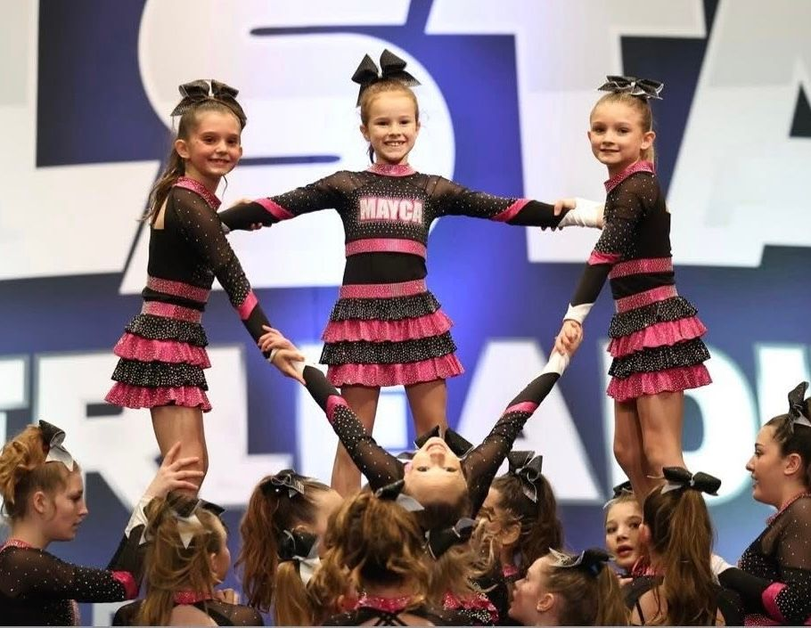 Cheerleaders in black and pink uniforms forming a pyramid during a competition.