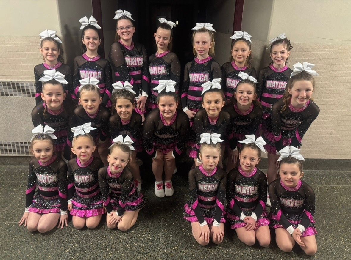 Cheerleading team in black and pink uniforms with white bows, posing together.