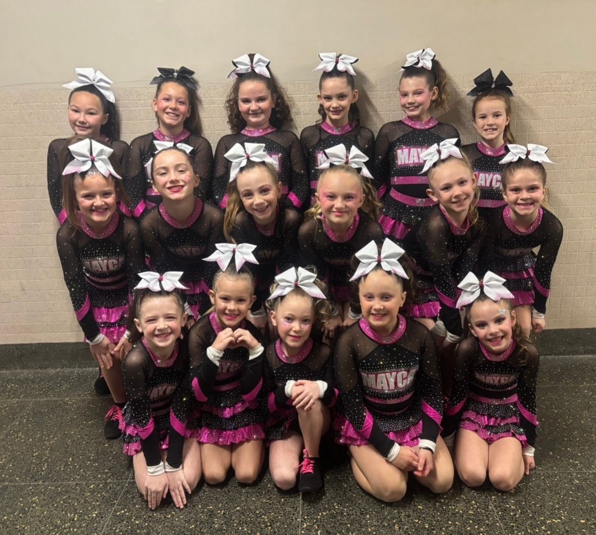 Cheerleading team posing in black and pink uniforms, white bows in their hair.