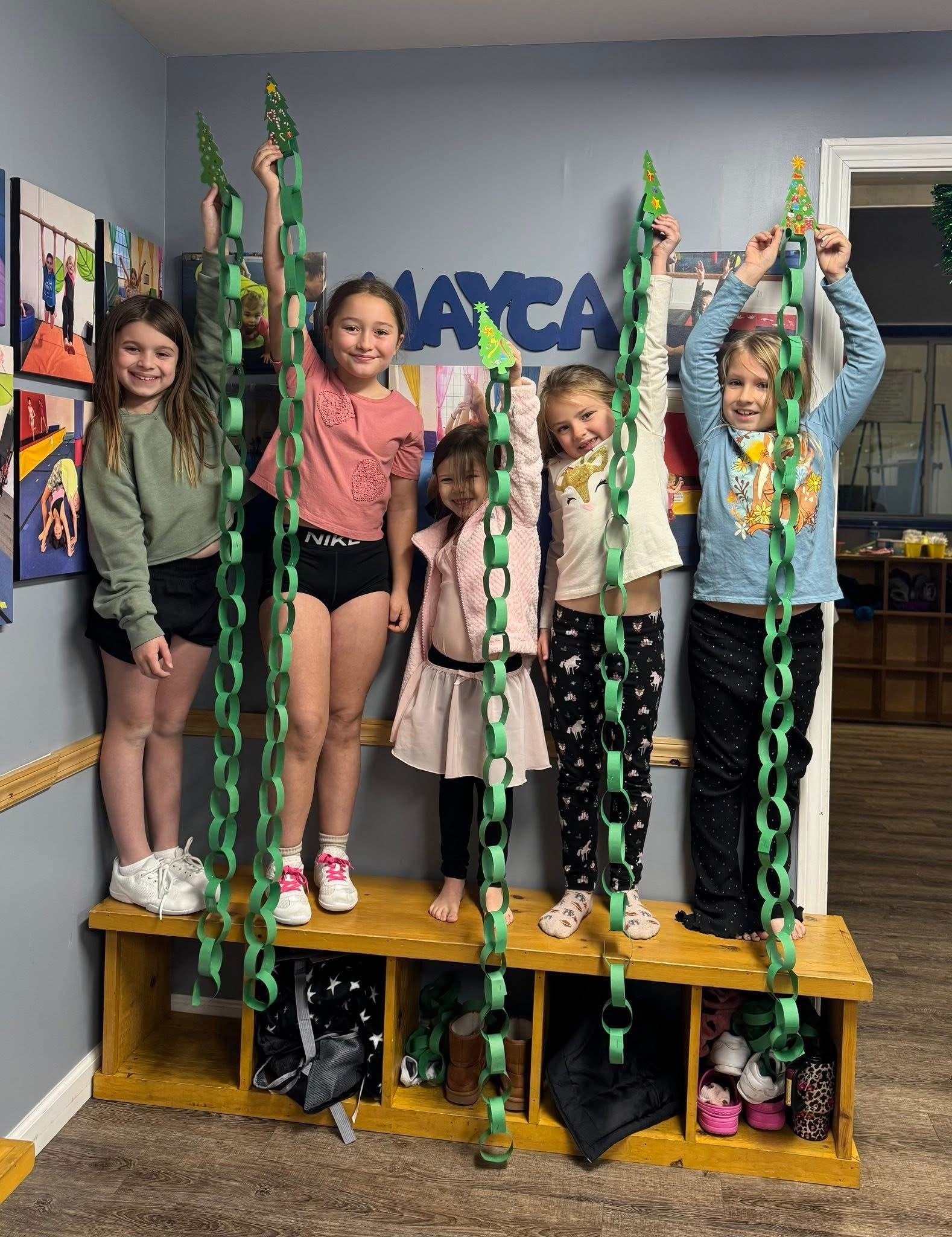 Five children holding up green paper chains in a classroom.
