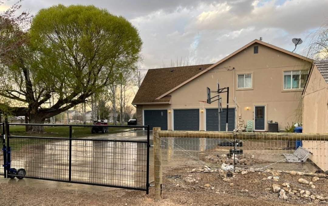 Exterior painting of a house with a fence in front of it and a tree in the background. Exterior painting in Idaho