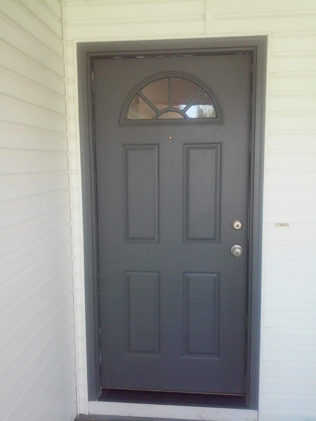A gray door with a window on it is on a white house.