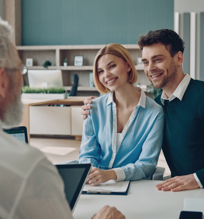 Couple smiles with arm around each other, meeting with a person over a desk.