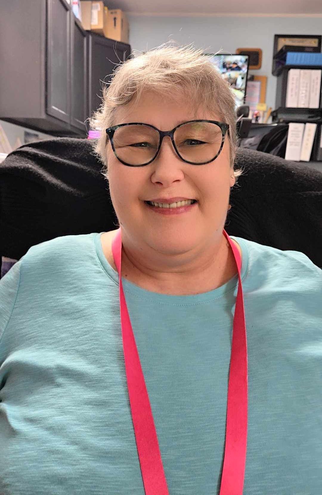 A woman wearing glasses and a floral shirt is smiling for the camera.