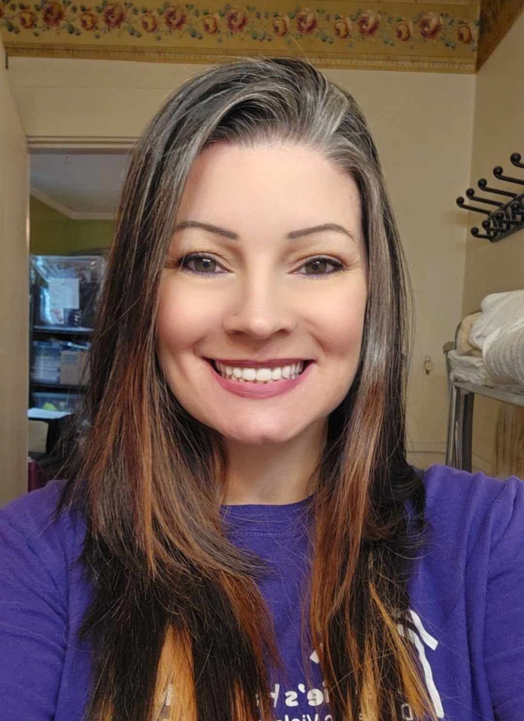 A woman with long hair is smiling for the camera in an office.