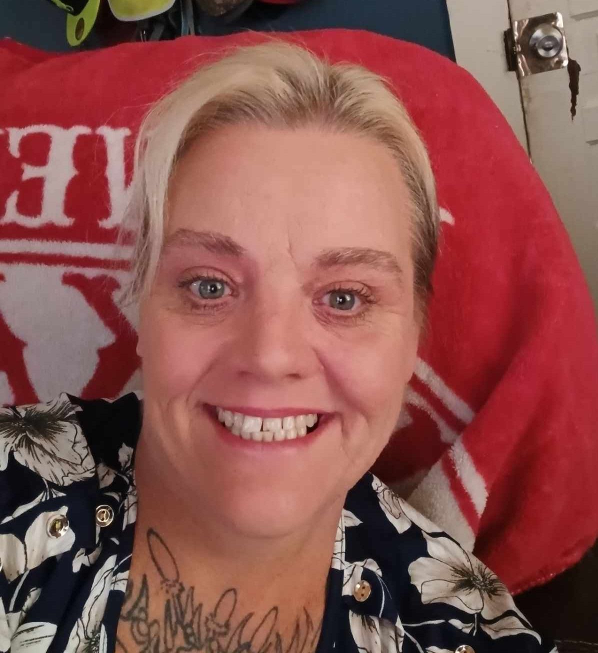 A woman with blonde hair and a tattoo on her chest is smiling.