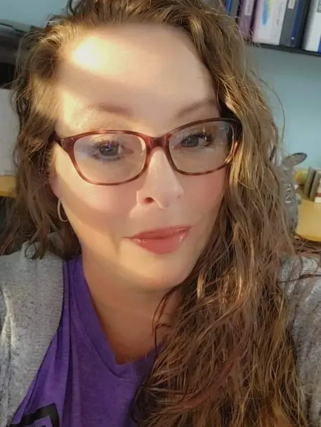 A woman wearing glasses and a purple shirt is taking a selfie.