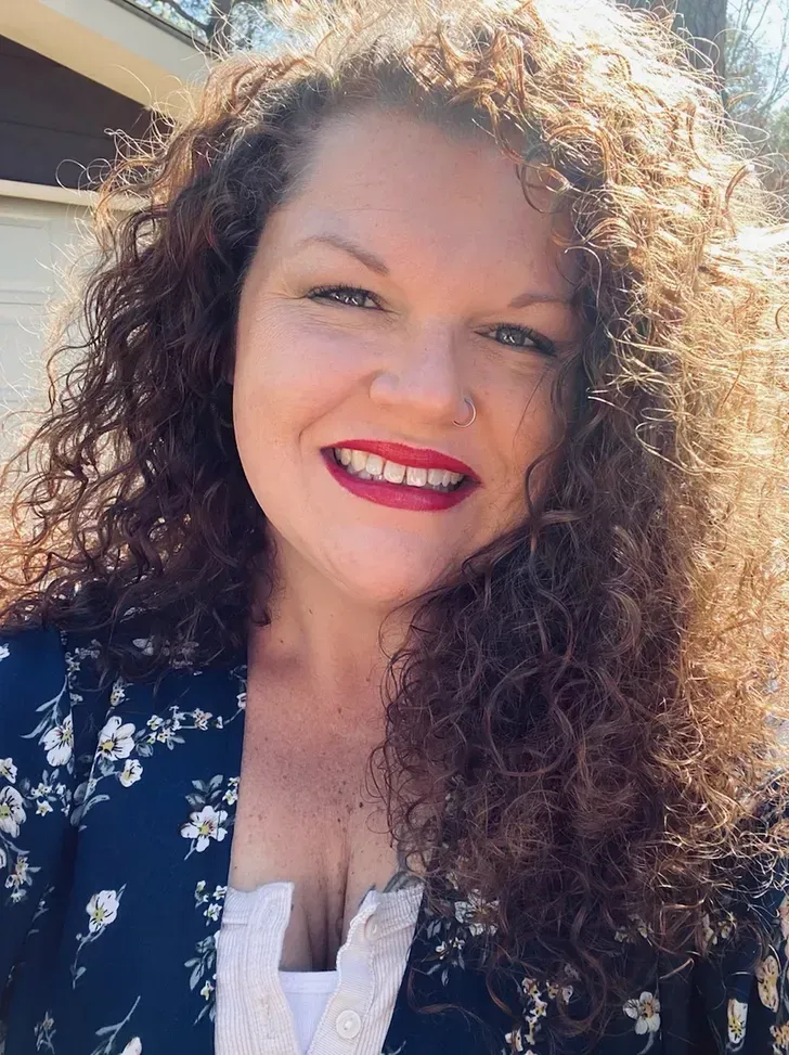 A woman with curly hair and red lipstick is smiling for the camera.