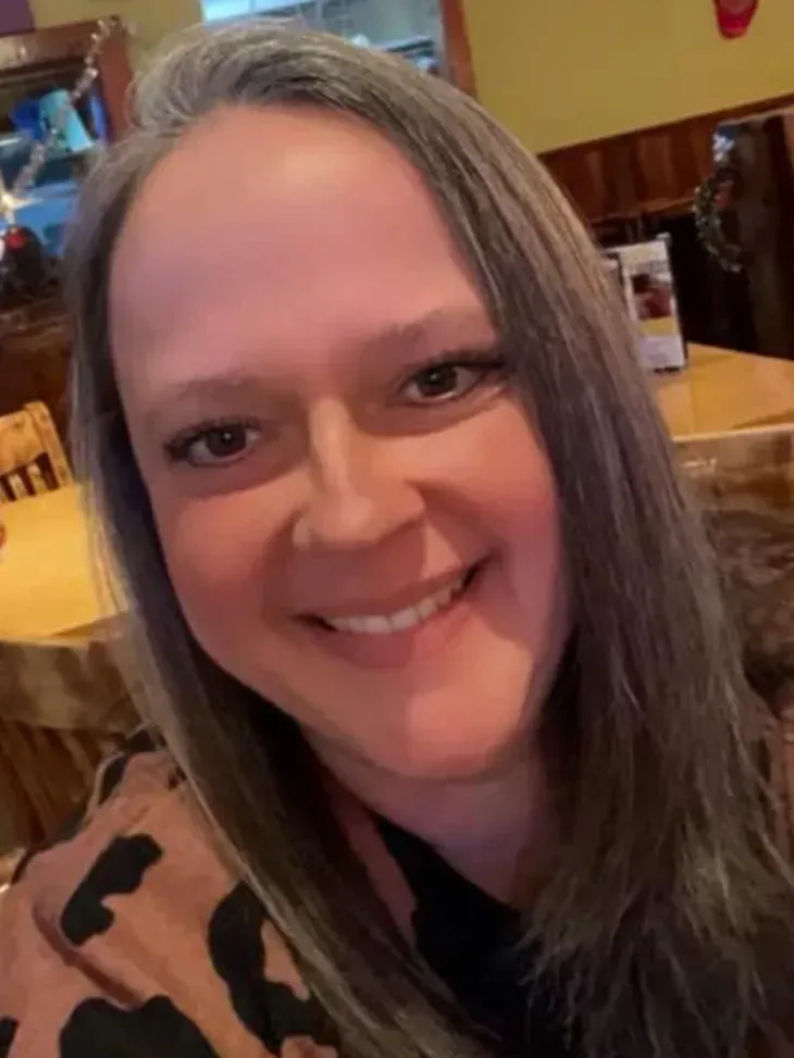 A woman is smiling for the camera while sitting at a table in a restaurant.
