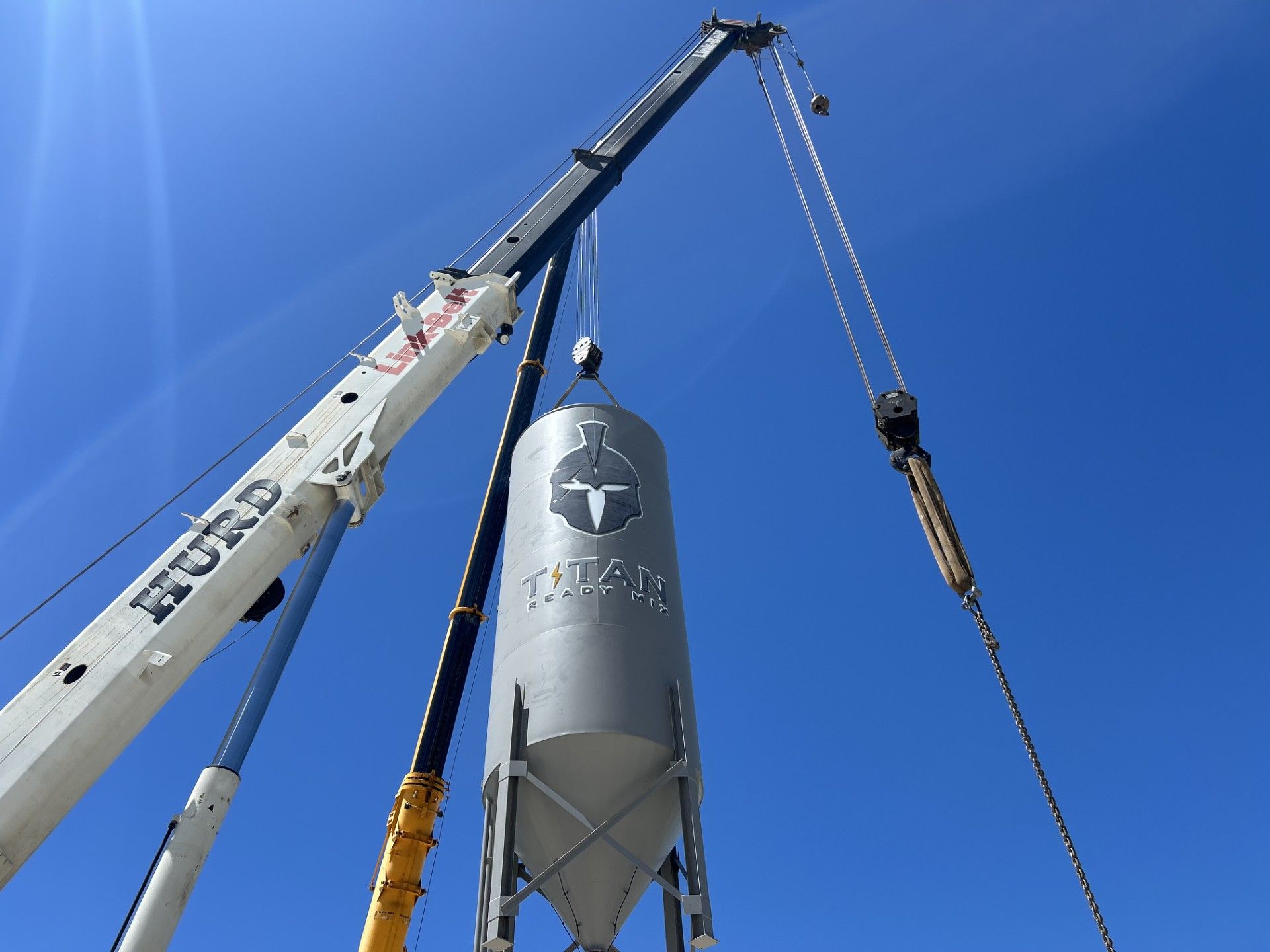 A crane lifting a large, gray industrial silo against a clear blue sky.