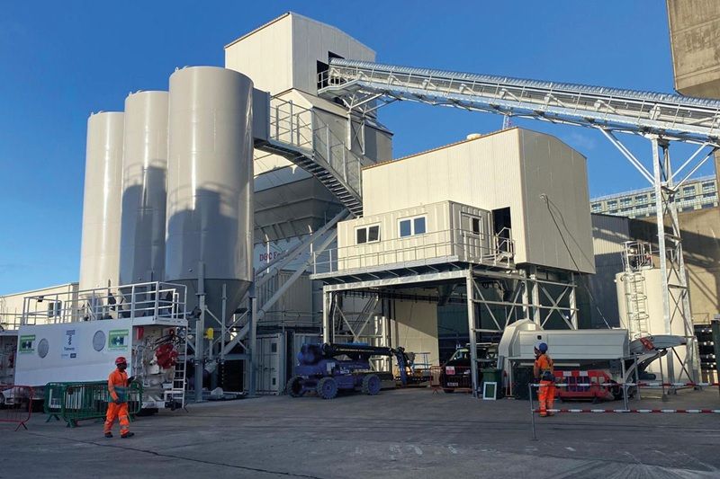 Concrete batching plant with silos, conveyor belts, and workers in safety vests.