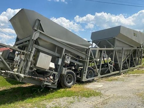 Gray industrial concrete batching plant on a trailer, outdoors on a grassy area.