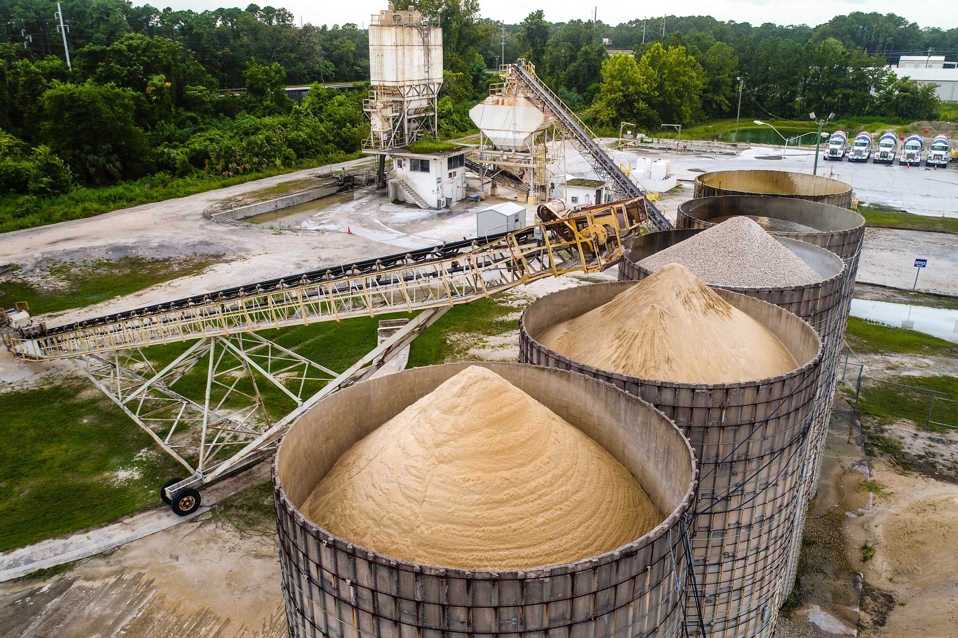Industrial site with silos overflowing with sand, conveyor belts, and machinery; outdoors.