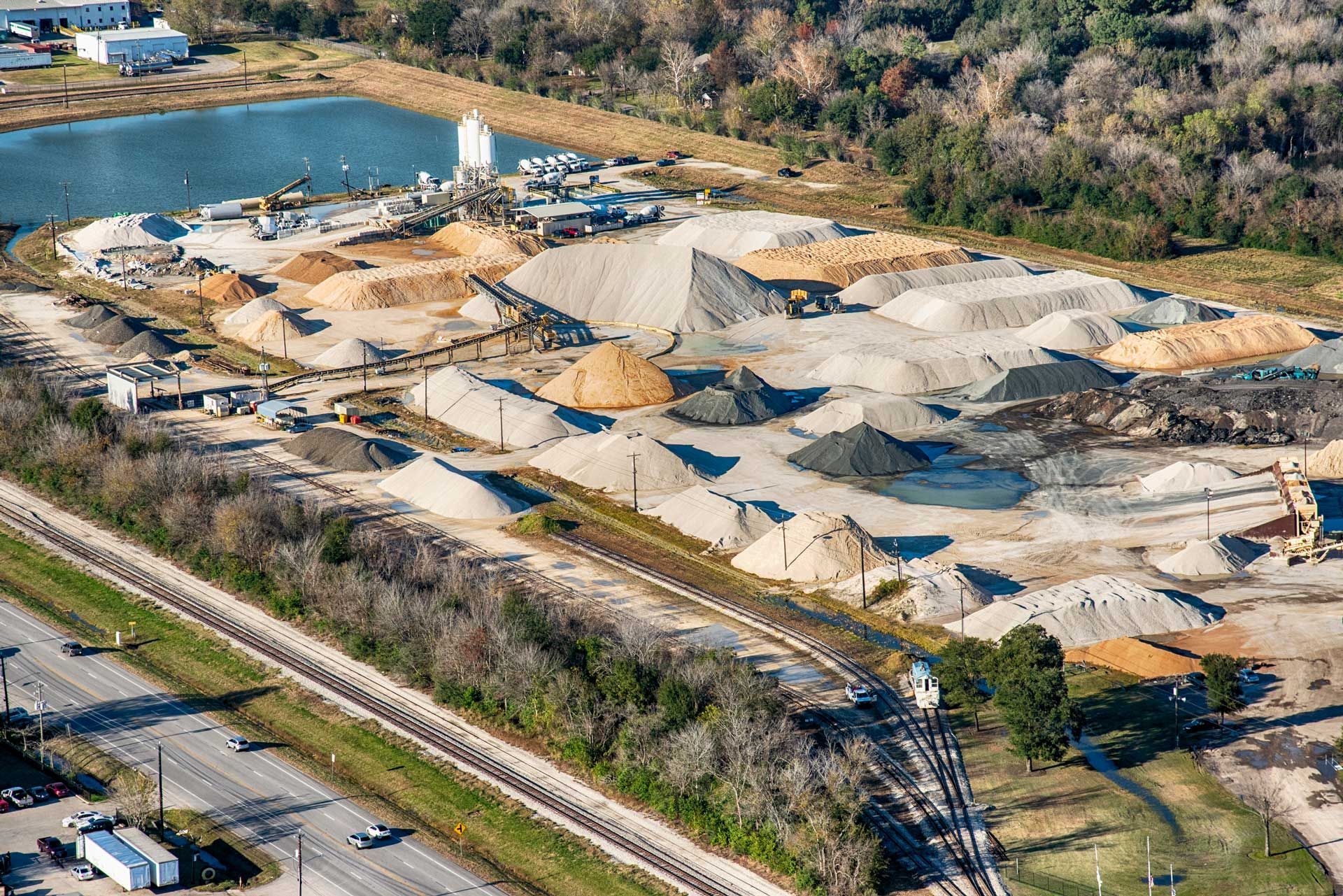 Aerial view of a sand and gravel plant with piles of material, a pond, and a highway.