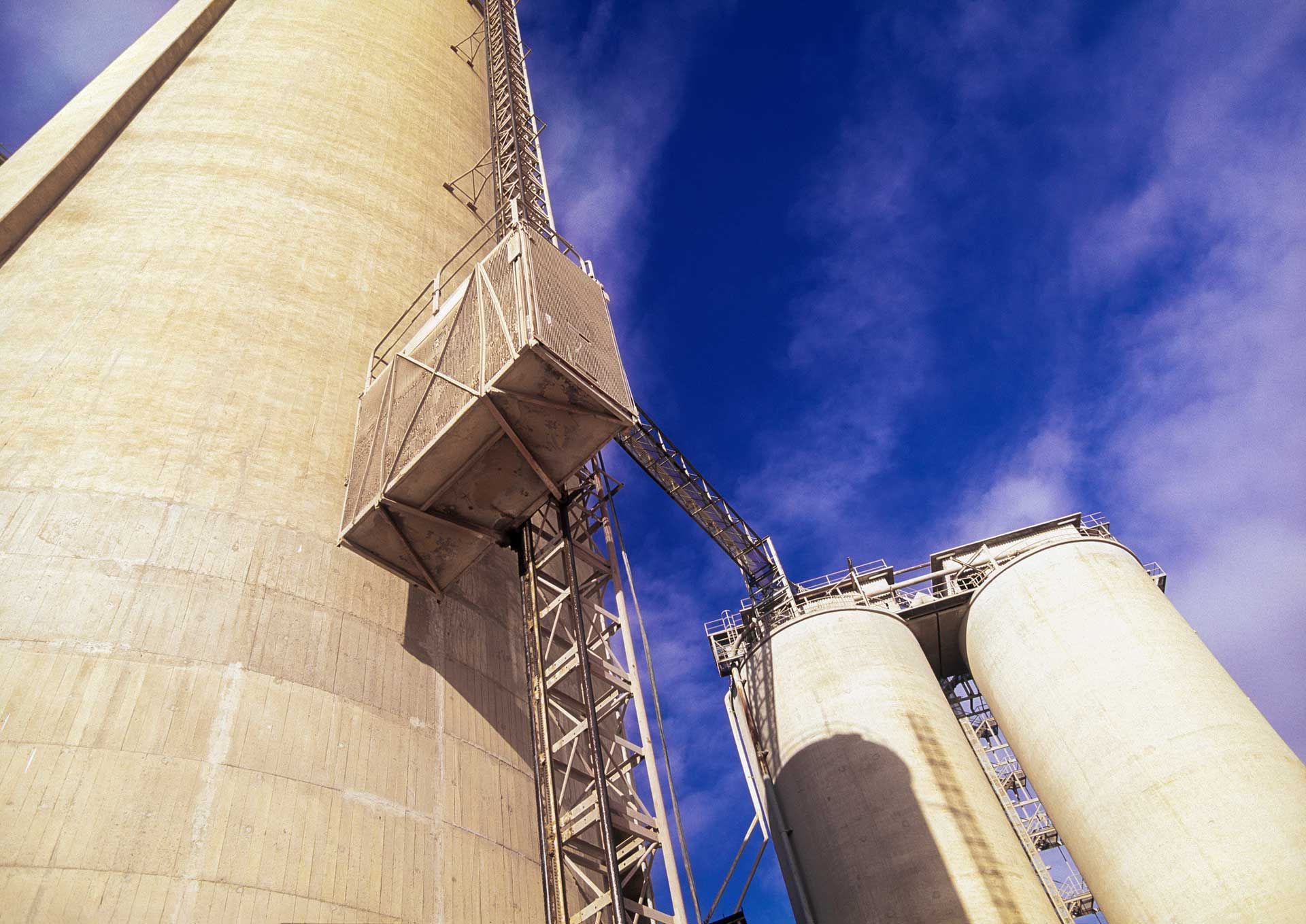 Tall concrete silos with metal conveyor system against a blue sky.