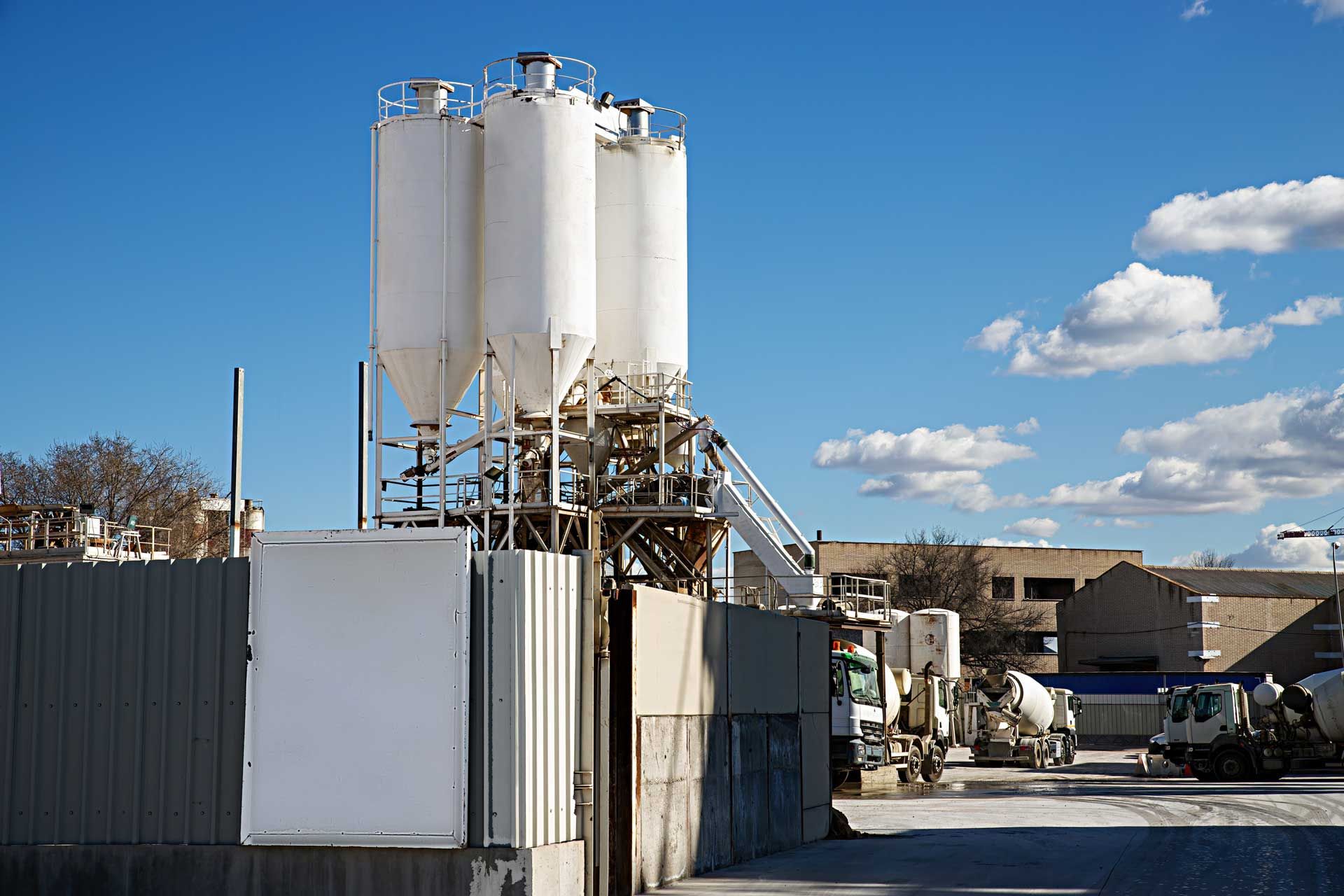 Cement plant with silos, conveyor, and ready-mix trucks against a blue sky.