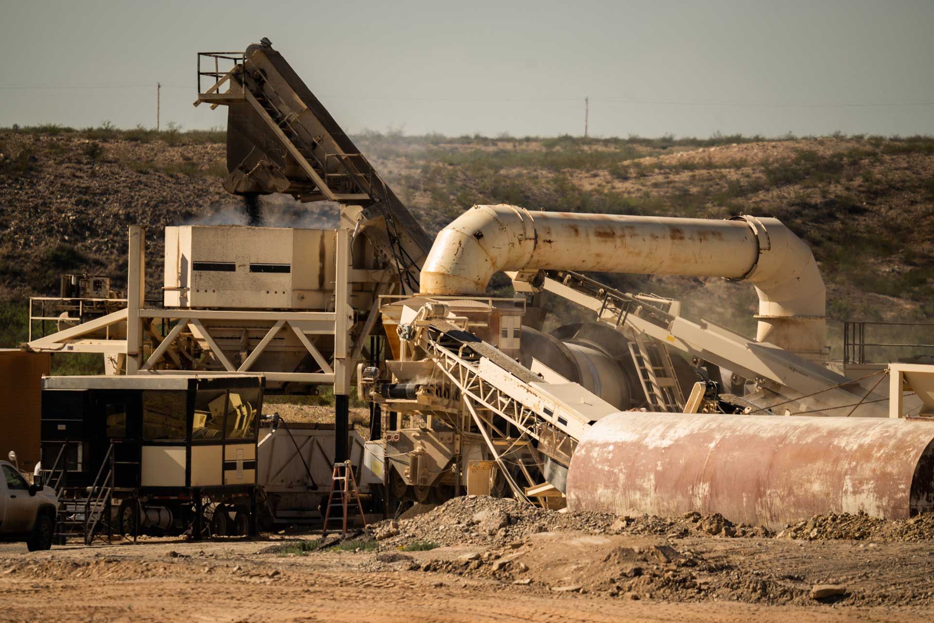 Mining equipment with conveyor belts, pipes, and structures in a quarry setting.