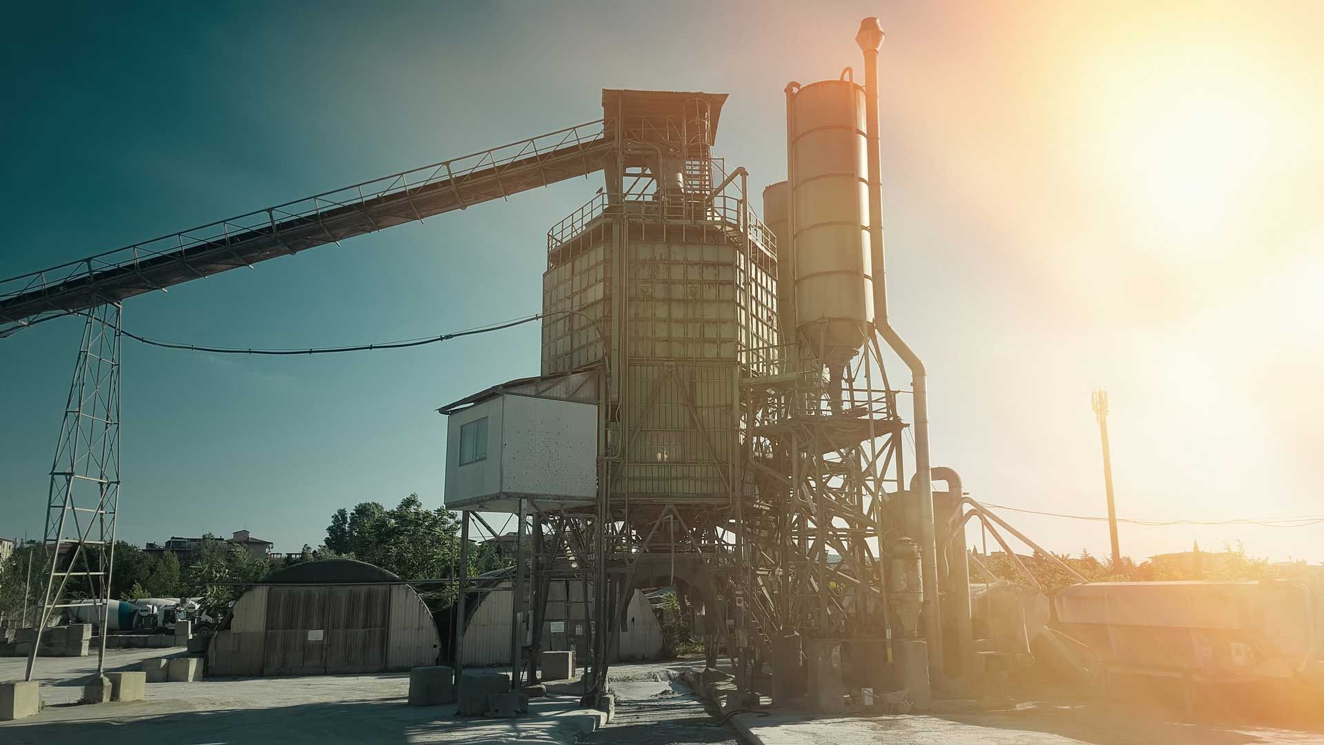 Cement factory with silos, conveyor belt, and bright sunlight.