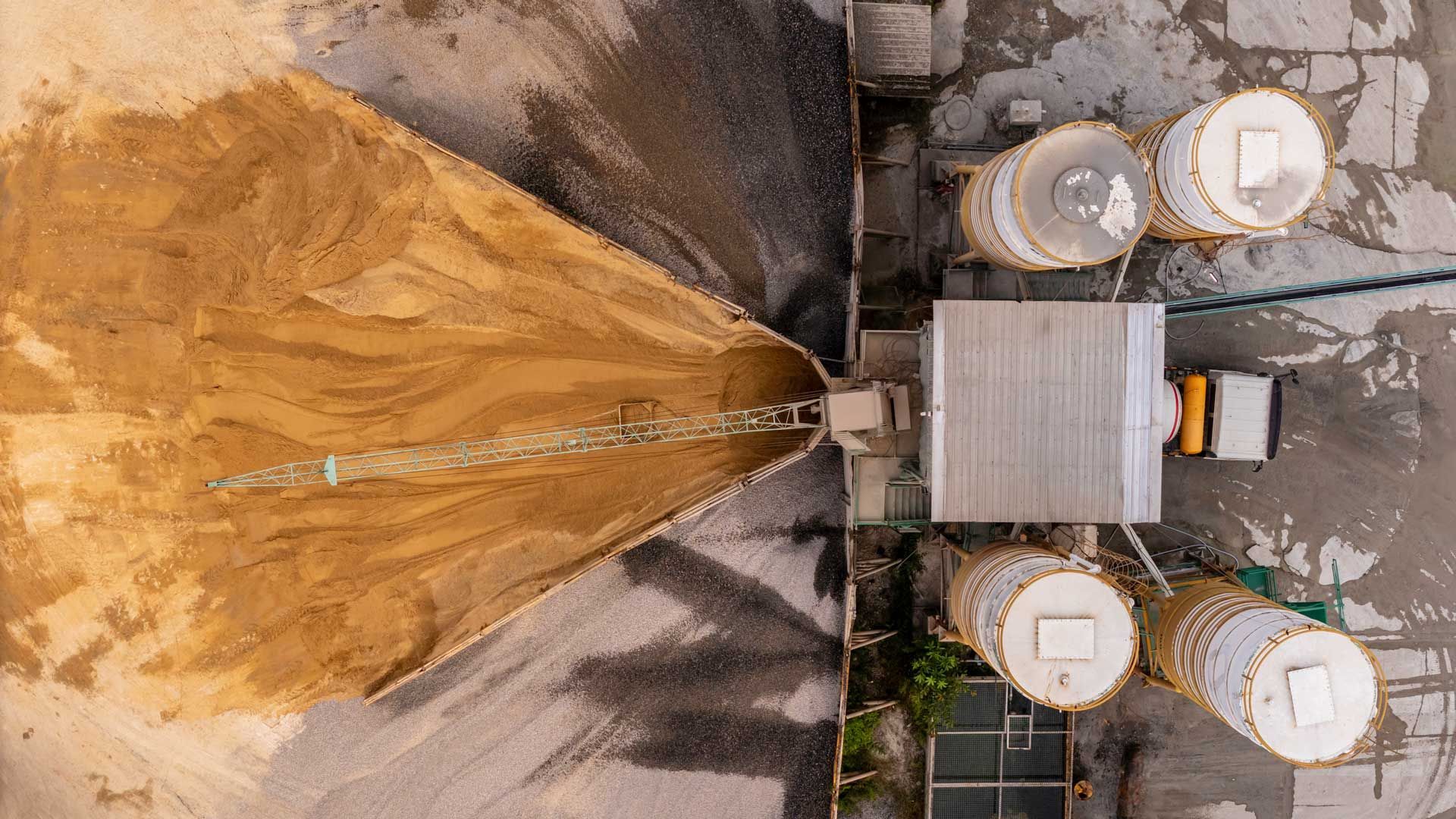 Aerial view of a sand pile and cement silos at an industrial site.
