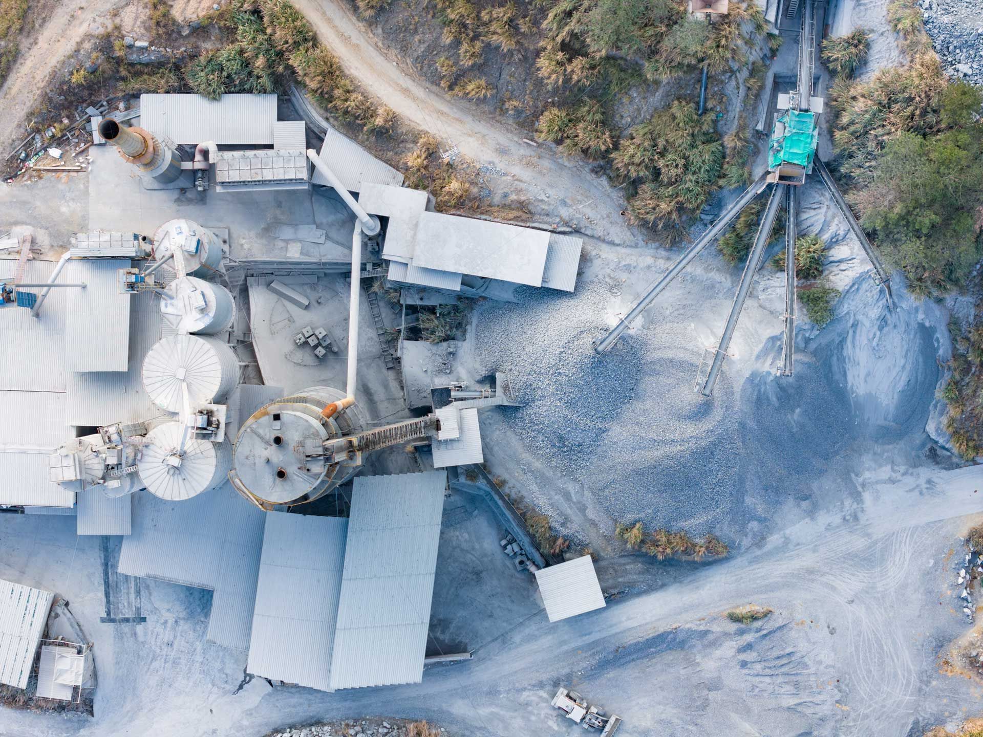 Overhead view of a quarry operation with buildings, conveyor belts, and piles of gravel on a rocky landscape.