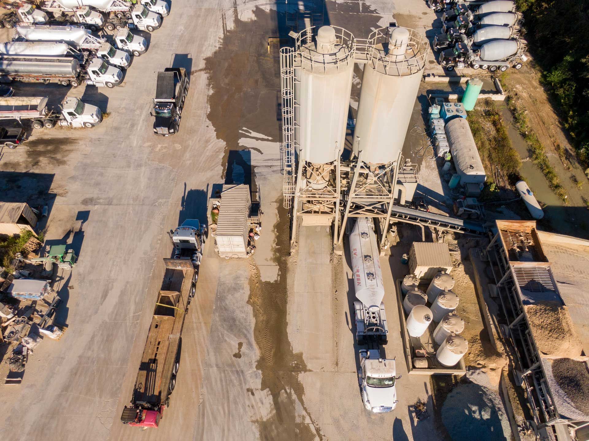 Aerial view of a concrete plant with silos, trucks, and equipment on a paved lot.