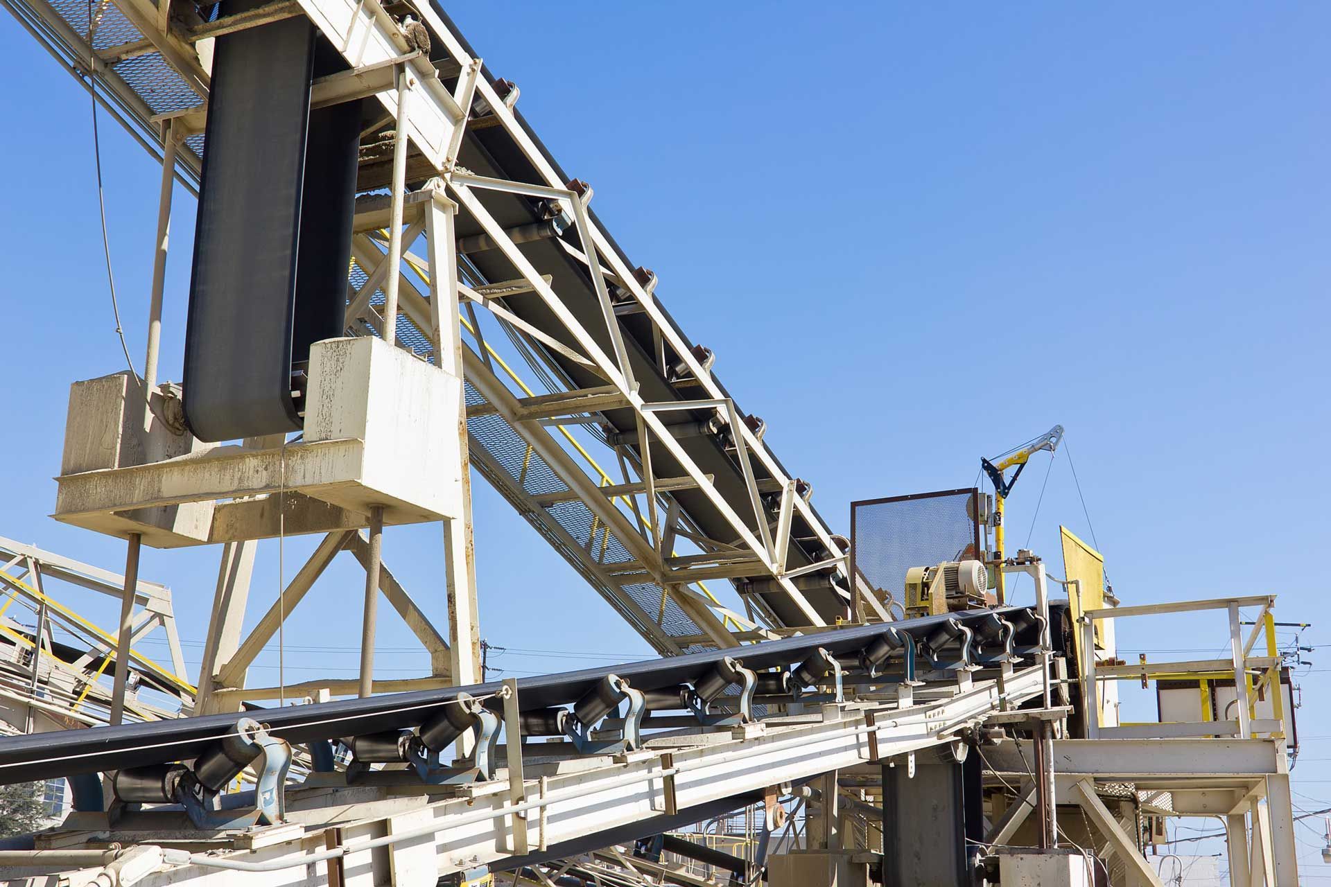 Elevated conveyor belt system against a clear blue sky, likely in an industrial setting.