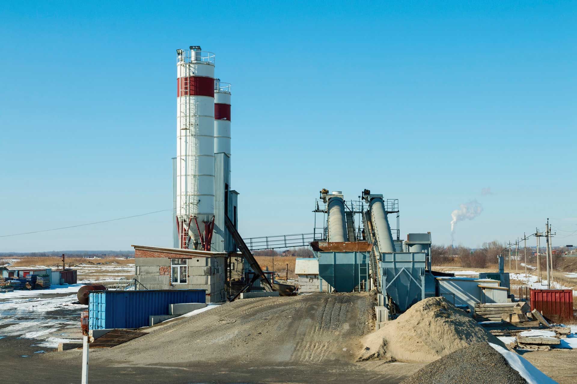 Concrete plant with tall white silos and machinery, set against a clear blue sky.