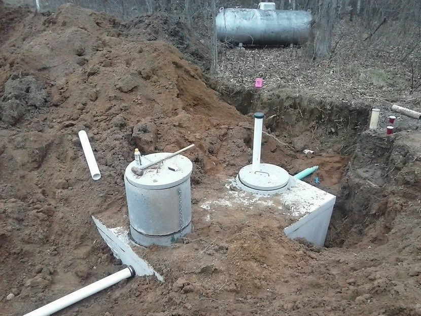 Underground utility pit with two gray cylindrical tanks, white pipes, and soil excavated around them.