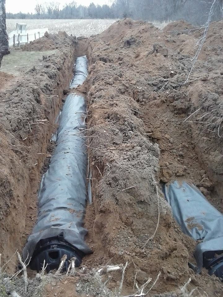 Trench with large black pipes laid underground at a muddy construction site.