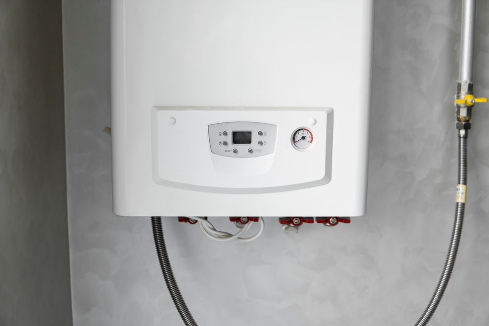 A wall-mounted white combi boiler with a digital display and pressure gauge, attached to pipes against a grey wall — GPE Plumbers In Kendall, NSW