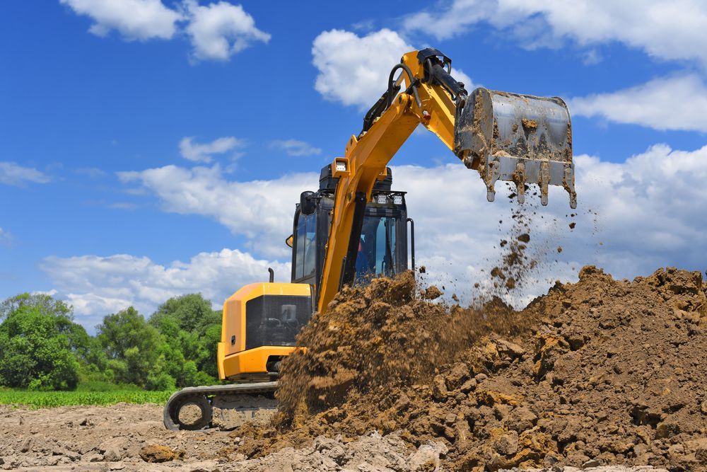 A Yellow Excavator Sits in a Field Under a Bright Blue Sky — GPE Plumbers In Kendall, NSW