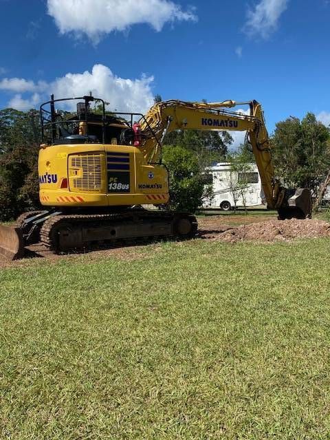 An Orange Excavator Sits in a Grassy Field With a Line of Trees — GPE Plumbers In Kendall, NSW