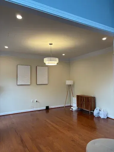 Empty living room with hardwood floors, beige walls, recessed lights, and a hanging ceiling fixture.