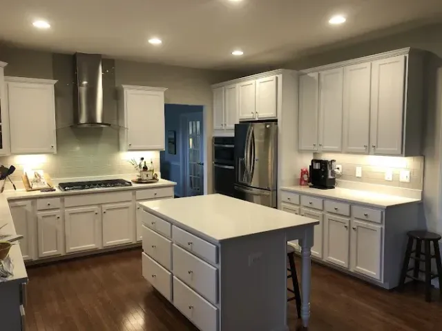 Bright modern kitchen with white cabinets, stainless fridge, island, and recessed ceiling lights