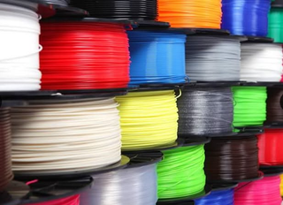 Persona con guanto blu che pulisce una superficie metallica con una spugna, sullo sfondo un contenitore rosa di sostanze chimiche.