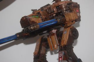 Persona con guanto blu che pulisce una superficie metallica con una spugna, sullo sfondo un contenitore rosa di sostanze chimiche.