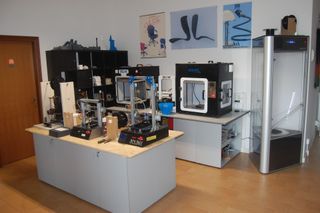 Persona con guanto blu che pulisce una superficie metallica con una spugna, sullo sfondo un contenitore rosa di sostanze chimiche.