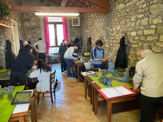 Persona con guanto blu che pulisce una superficie metallica con una spugna, sullo sfondo un contenitore rosa di sostanze chimiche.