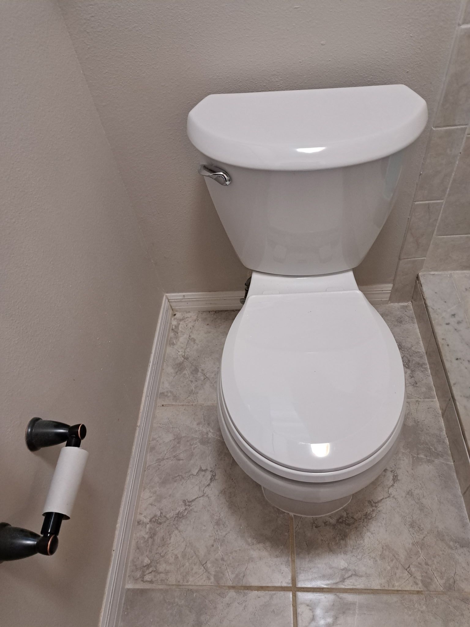 A white toilet is sitting on a tiled floor in a bathroom.