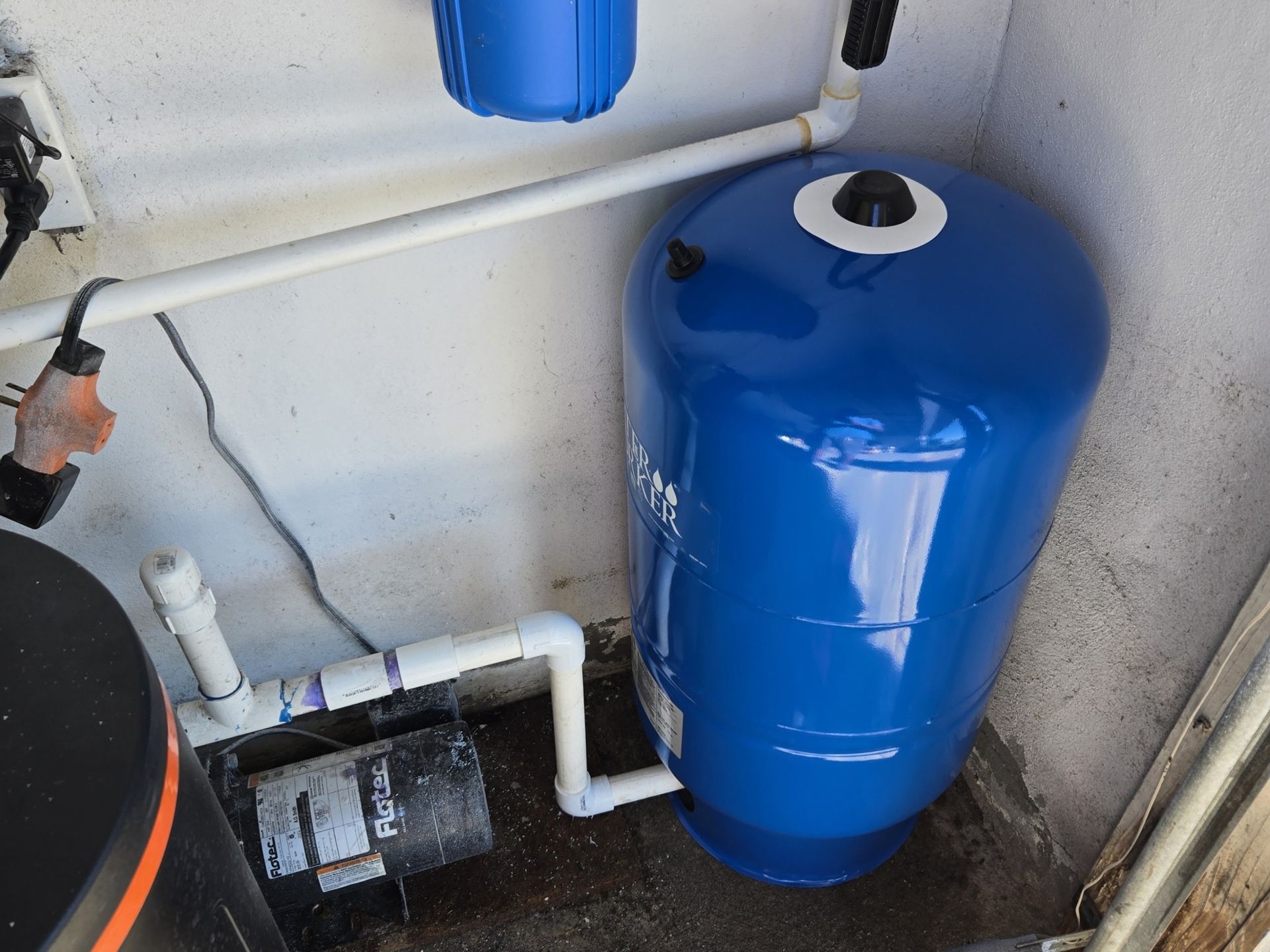 A blue water tank is sitting in a room next to a pump.