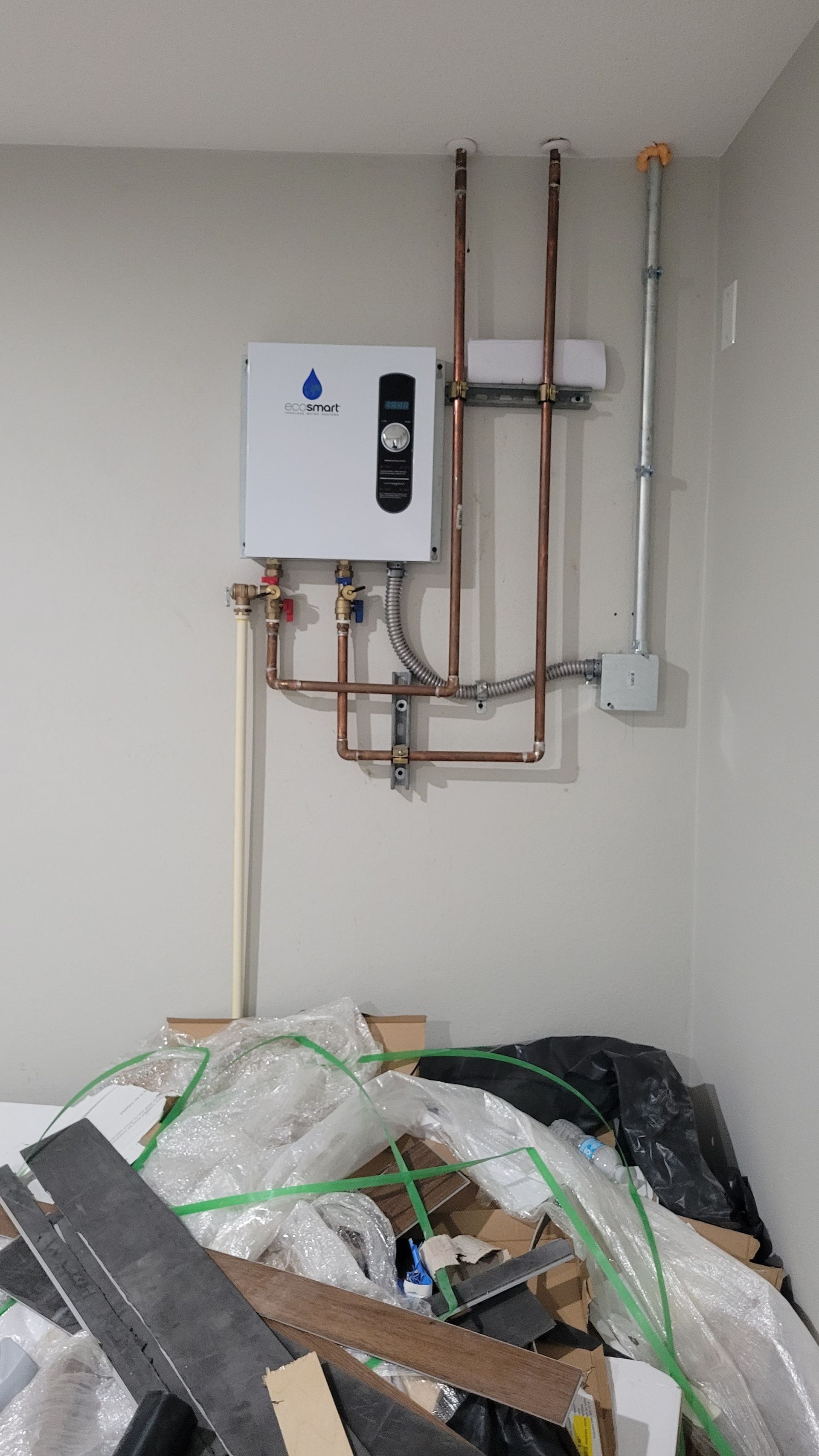 A room with a water heater and pipes on the wall.