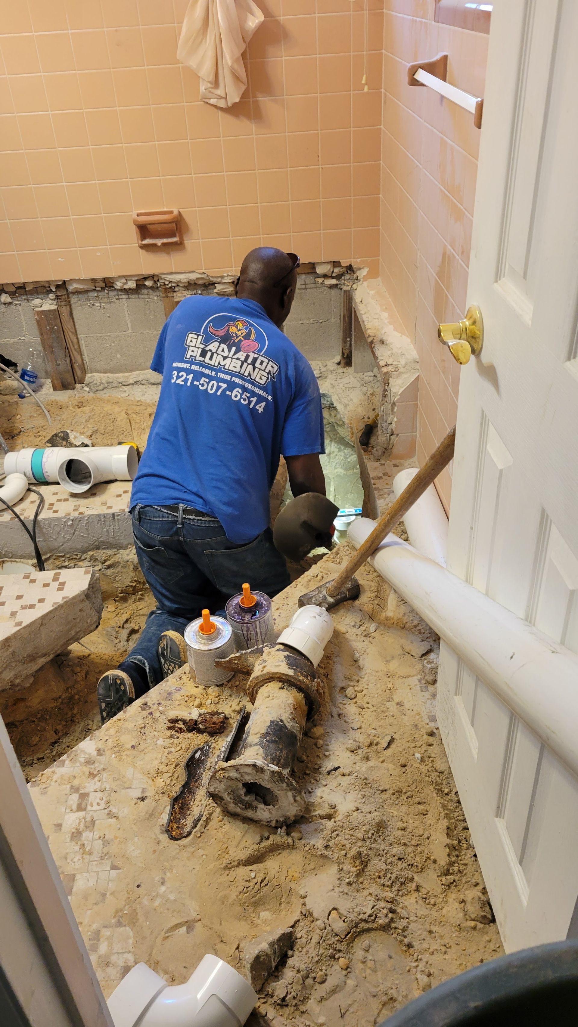 A man in a blue shirt is working in a bathroom.